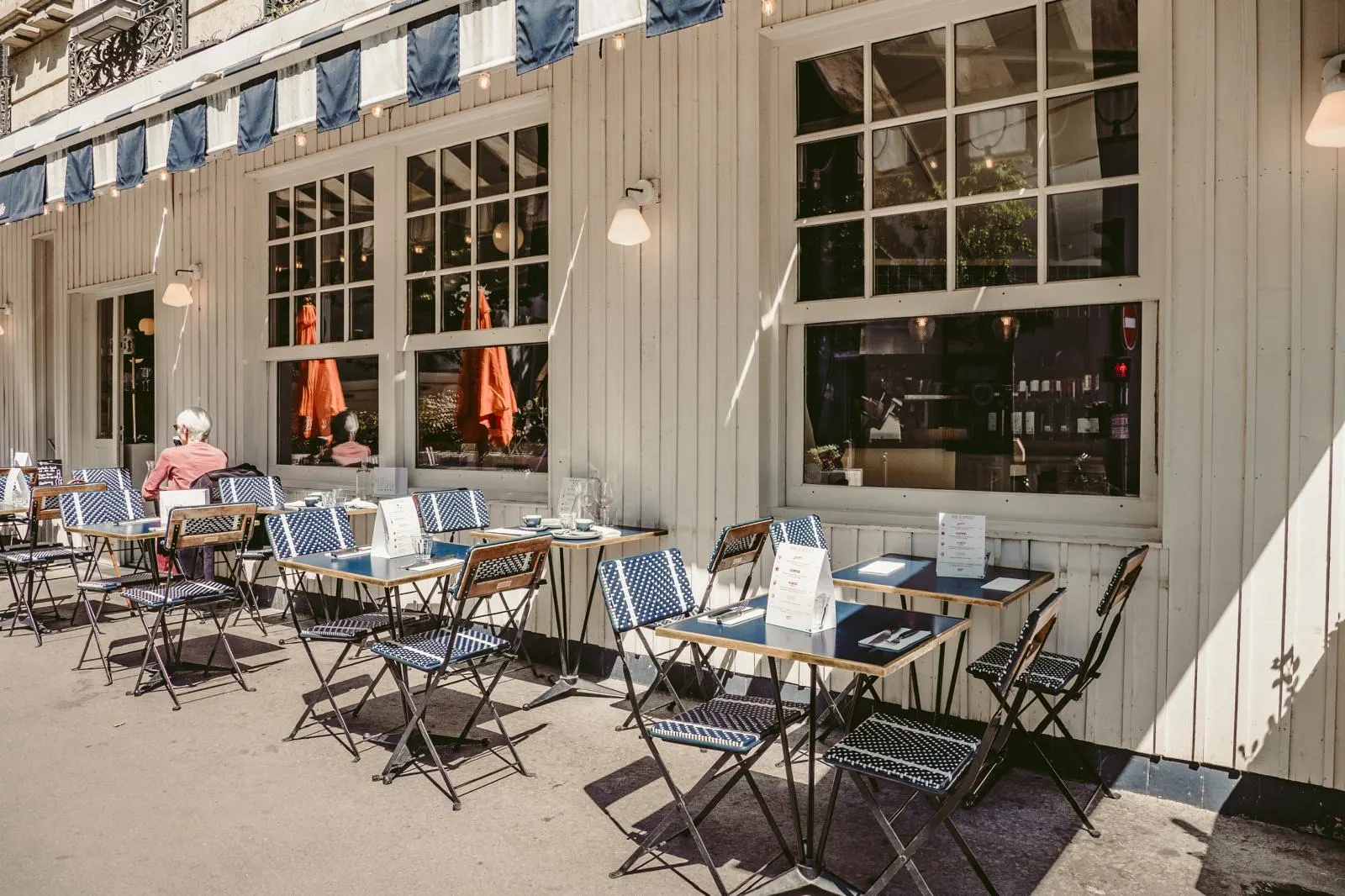 La terrasse en enfilade le long de la façade crème et des stores rayés