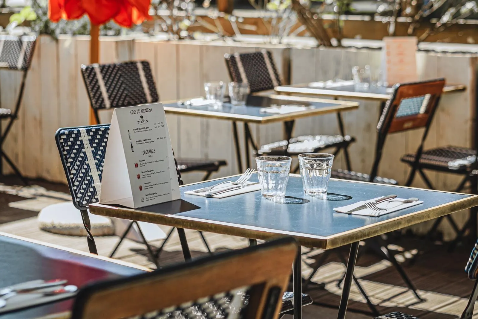 Tables bleues à chant laiton et chaises tressées sur la terrasse ensoleillée