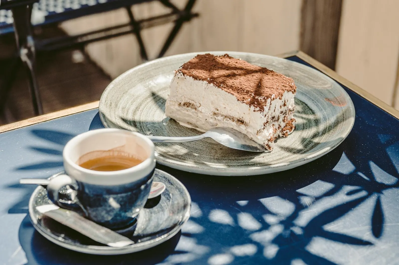 Une part de tiramisù et un espresso sur une table bleue en terrasse